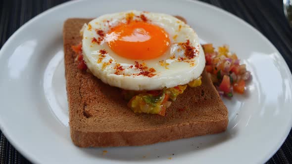 Closeup of a Round Shaped Roasted Egg with Raw Vegetables on a Whole Grain Bread on a White Plate
