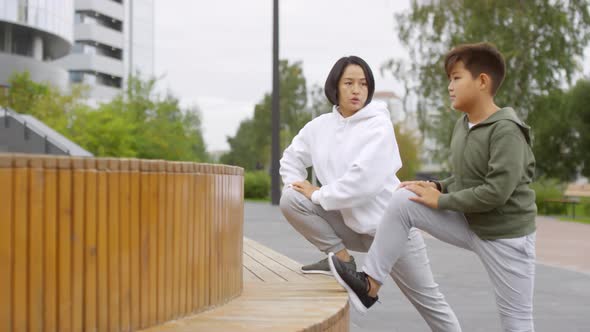 Asian Mother and Son Stretching Legs during Outdoor Workout alt