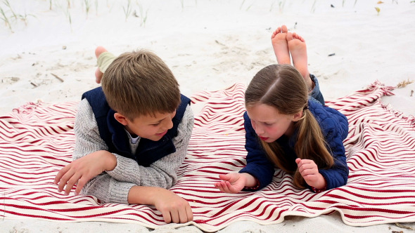 Siblings Lying On Blanket On The Beach Talking