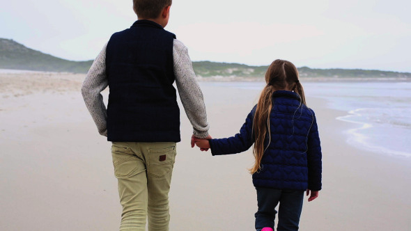 Siblings Walking Hand In Hand On The Beach