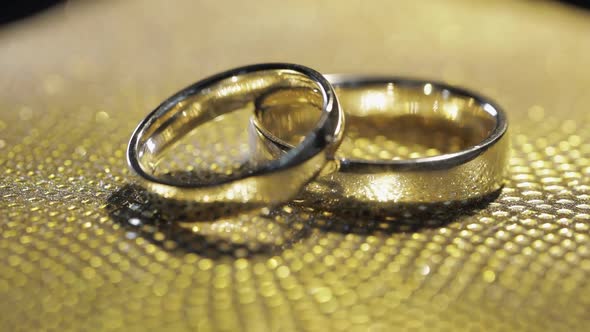 Wedding Rings Lying Rotate Spinning on Shiny Golden Shining Surface with Light Closeup Macro alt