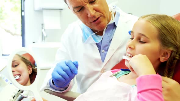 Dentist assisting young patient while brushing teeth alt