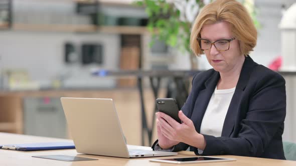 Old Businesswoman Using Smartphone and Laptop in Office  alt