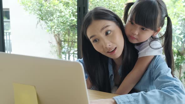 Young Asian dad enjoys teaching his lovely daughter do a homework on a laptop. alt