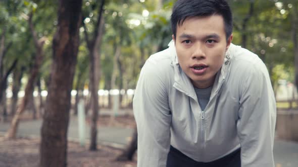 Handsome Asian man athlete runner resting exhausted after exercise training outdoors in the forest.