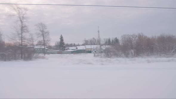 The Train Passes Through the Countryside with Snowcovered Buildings and Trees