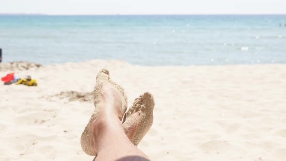 Closeup of Men's Feet on a Sandy Beach Against a Background of Azure Sea and Blue Sky