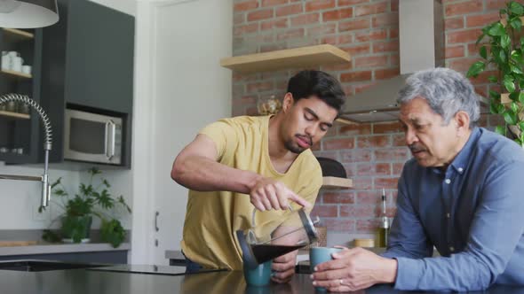 Young man pouring fresh black coffee in mug for father at kitchen counter alt