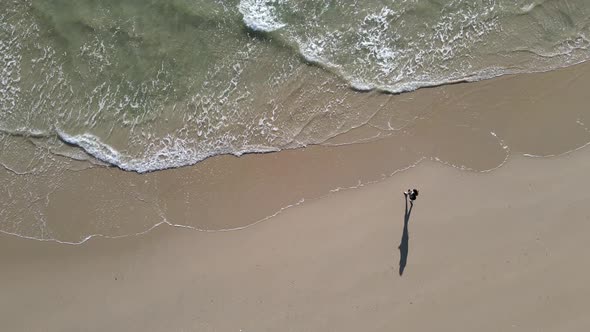 Aerial View of Person Walking on Beach with Waves Crashing in