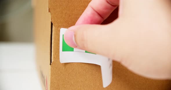Hands applying MADE IN NIGERIA flag label on a shipping cardboard box with products. Close up shot w alt