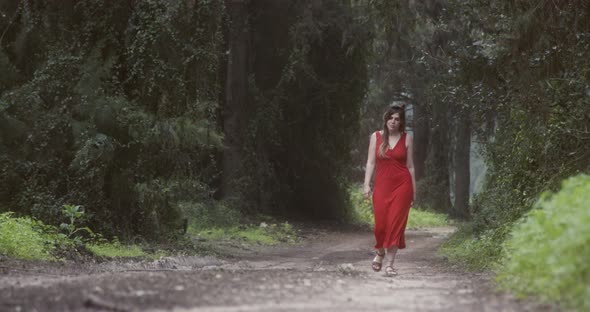 Young beautiful woman with a red dress walking in a green forest