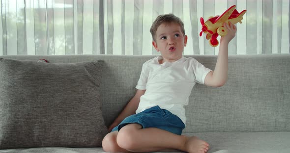 A Cute Little Preschooler Boy Playing at Home on the Sofa with a Toy Airplane a Cute Little Son alt