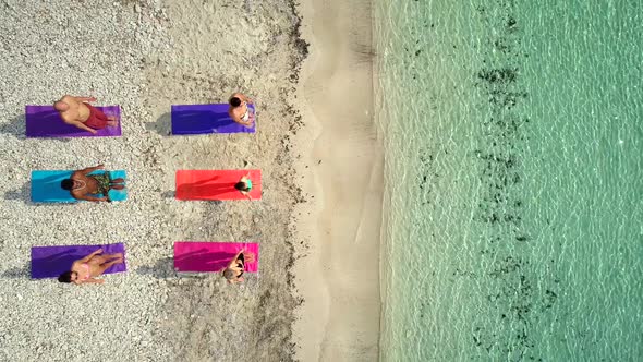 Aerial view of group of people doing yoga on colorful mats on sandy beach. alt
