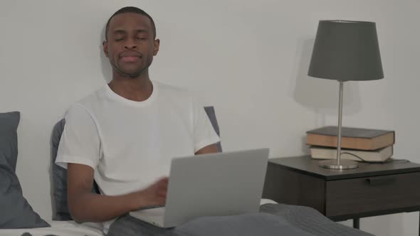 African Man Showing Thumbs Up Sign While Using Laptop in Bed alt