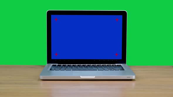 Blue screen laptop computer sitting on wooden desk with chroma key green screen