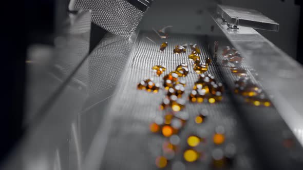 Yellow Gel Capsules Move on the Conveyor Belt of the Medical Machine alt
