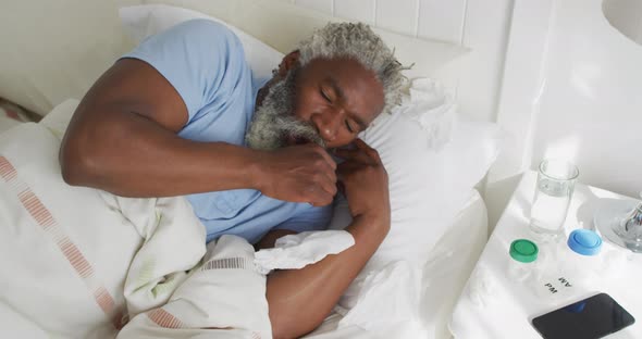 Senior man with tissue coughing in the bed at home alt
