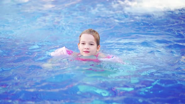 a Funny Little Girl Swims in Inflatable Armbands in a Pool alt