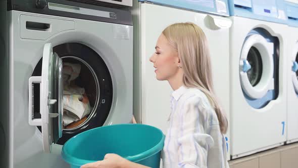 An Attractive Woman Picks Up Laundry From a Washing Machine in a Public Laundry Room alt