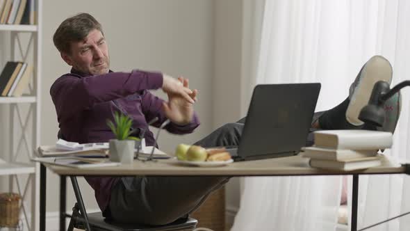 Wide Shot of Carefree Man with Feet on Table Stretching Hands and Legs Waiting for Virtual alt