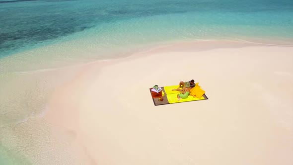Aerial drone view of a man and woman couple having a picnic meal on a tropical island beach alt