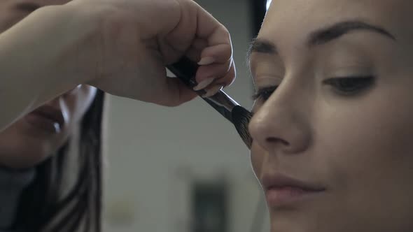 With a Special Makeup Brush a Professional Makeup Artist Makes Makeup for a Beautiful Female Model