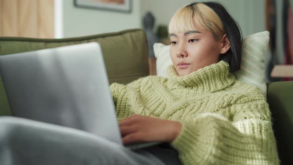 Confident Asian woman typing at laptop at home alt