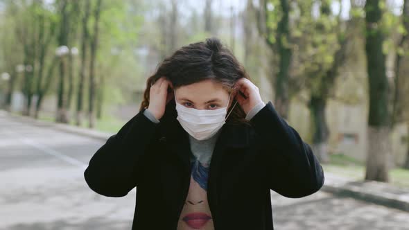 A Young Redhaired Girl Stands on the Street Puts on a Medical Mask