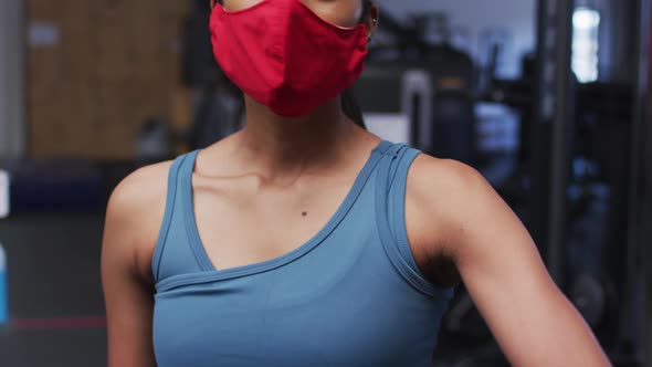 Fit caucasian woman wearing face mask sneezing on her elbow in the gym alt