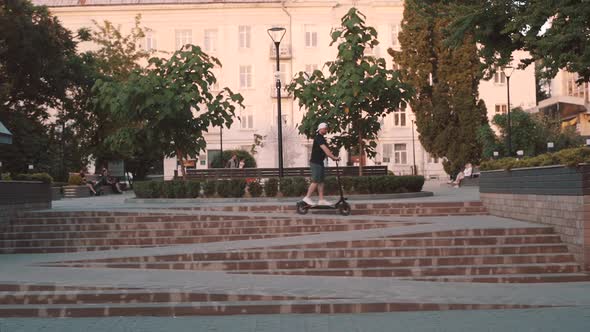 Slow Motion of Man in White Cap Riding Electric Scooter in City alt