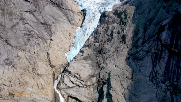 Glacier melting and forming a waterfall through a rocky mountain - Aerial footage alt