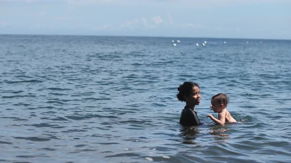 In the Deep Cool Sea a Young Darkhaired Woman Teaches Her Young Child to Swim Carefully