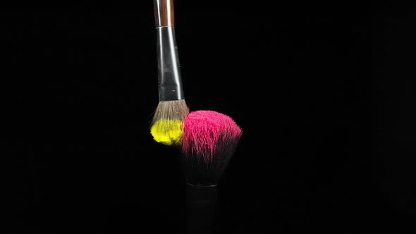 Makeup Brushes Touch Each Other on Black Dark Background and Small Particles of Color Cosmetics alt
