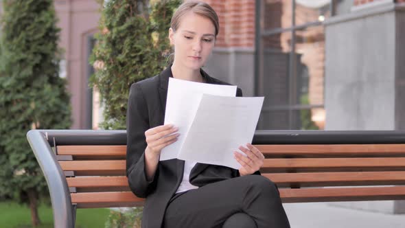 Young Businesswoman Reading Documents while Sitting Outdoor on Bench alt