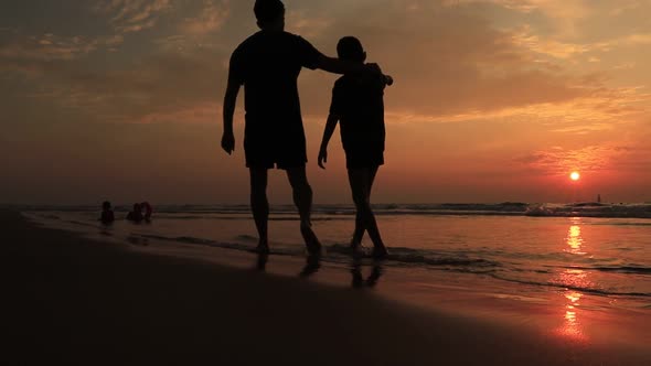 Father and Son Walk on the Beach at the Sunset Time