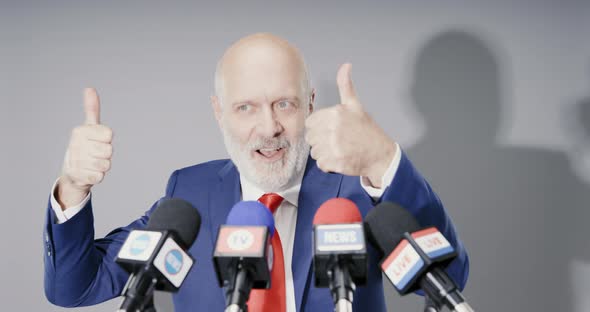 Politician greeting the audience before starting his speech, he is smiling with hands up