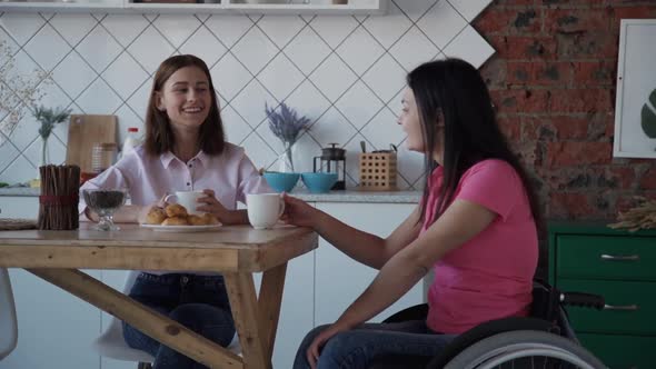 Disabled American Woman and Friend Talking at Table in Apartment Interior.