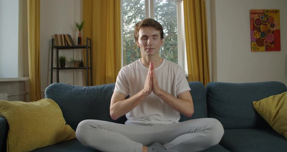 Young Man Meditating at Home with Closed Eyes Indoors Slow Motion. Front View of Caucasian Guy