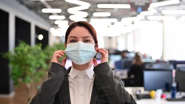 A Happy Female Office Worker in a Suit Takes Off Medical Mask alt