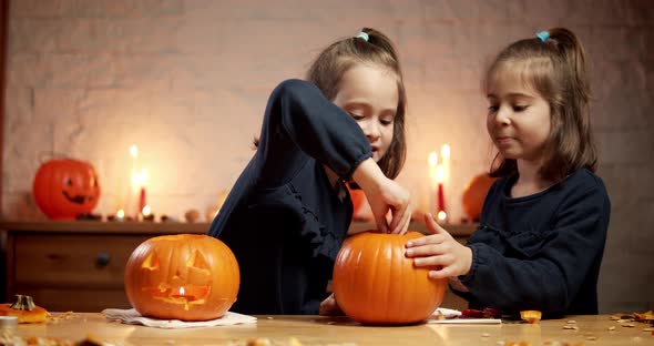 Two Cute Little Girls Are Cutting a Pumpkin on the Table for Halloween alt