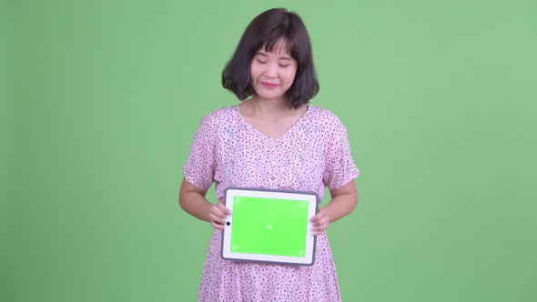 Happy Asian Pregnant Woman Thinking While Showing Digital Tablet alt
