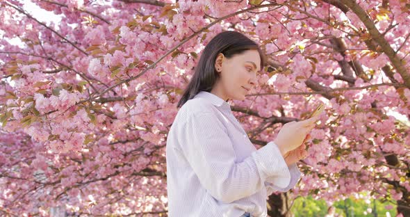 Girl standing at the sunny park and chatting with friends, using cellphone outdoors.  alt