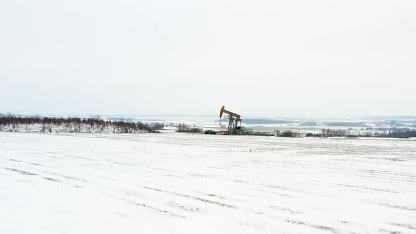 [DRONE] low push in shot of an oil derrick with a black car next to it, all covvered in snow alt