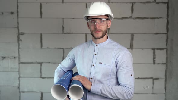 A construction engineer stands in front of the camera with blueprints in his hands alt