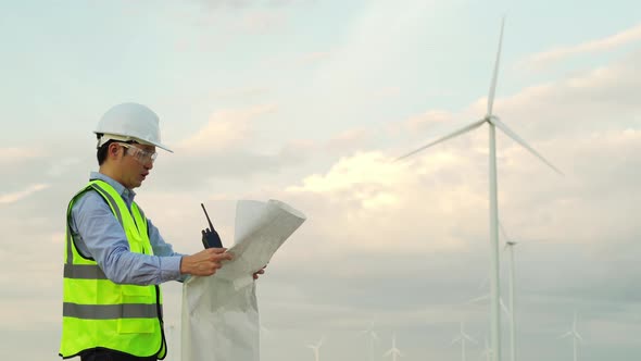 young male engineer analyze a blueprint drawing of wind turbine farm