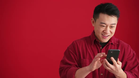 Surprised Asian man wearing shirt looking at phone and showing different gestures alt