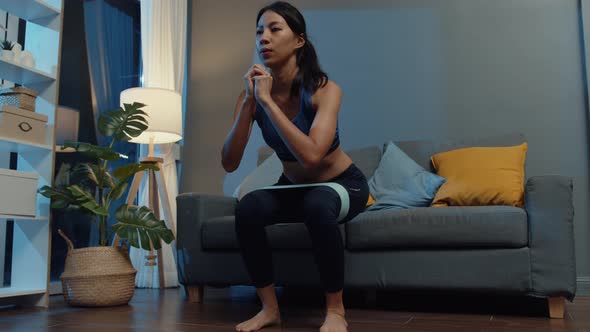 Asia lady in sportswear doing squat exercise working out in living room at home at night.