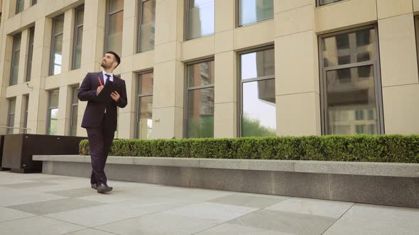 Young Businessman Walks Down the Street with a Tablet alt