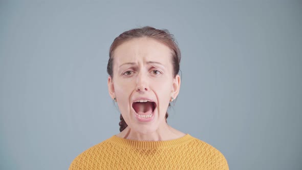 A beautiful middle-aged woman screams with her mouth wide open and looking at the camera. alt