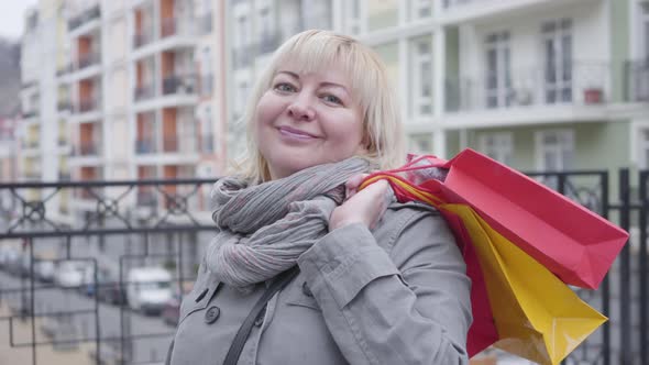 Close-up Portrait of Happy Senior Caucasian Woman Standing with Shopping Bags Outdoors. Nice alt